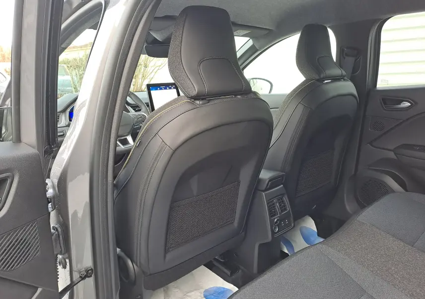 Vue intérieure arrière côté gauche du Renault Symbioz gris cassiopée, montrant les sièges avant en cuir noir et la console centrale.