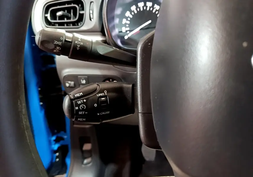 Gros plan sur la commande de régulateur de vitesse derrière le volant d'une Citroën C3 bleu 2017.
