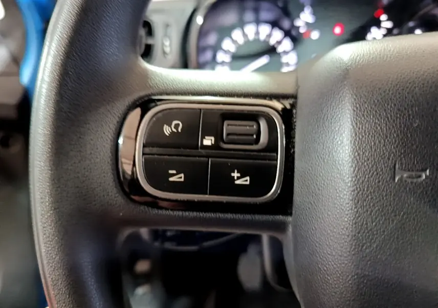 Gros plan sur les commandes du volant à gauche du Citroën C3 bleu, avec tableau de bord flou en arrière-plan.