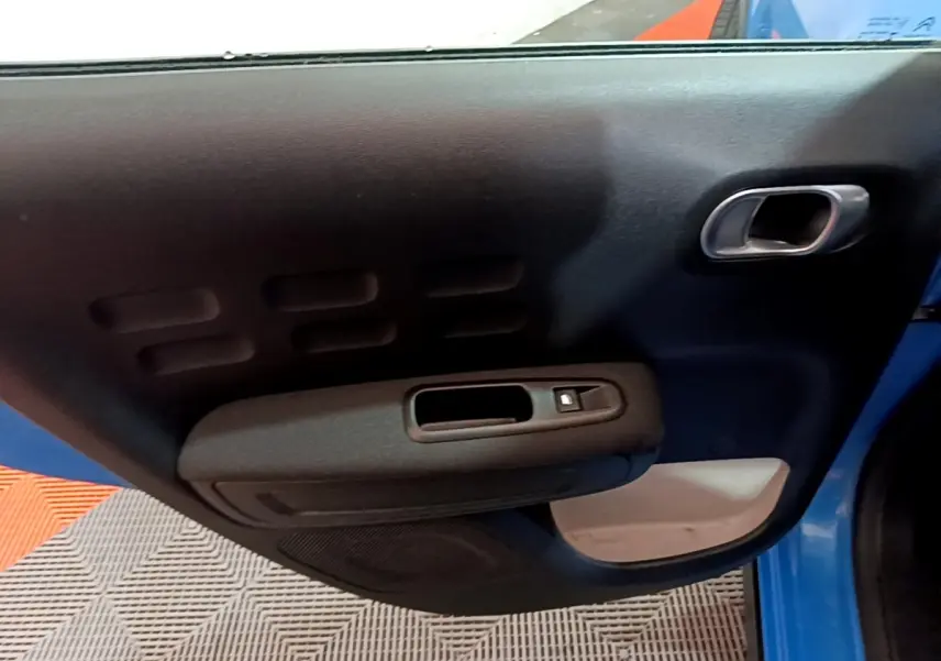 Vue rapprochée de la porte côté gauche bleu d'une Citroën C3 2017 avec poignée et commande de vitre électrique.