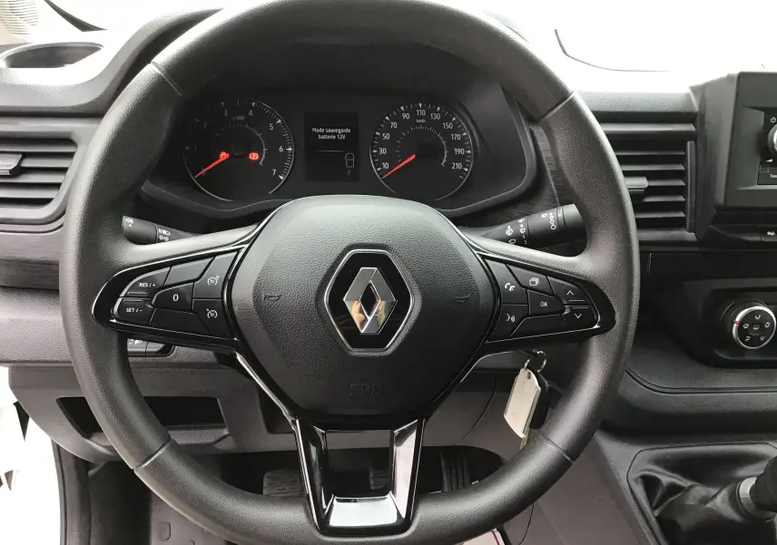 Vue rapprochée du volant noir du Renault Trafic Fourgon 2024 avec commandes intégrées et tableau de bord visible.