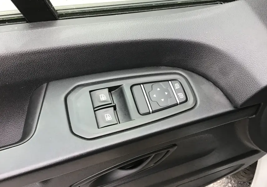 Gros plan sur les commandes de lève-vitres et réglage des rétroviseurs côté gauche d’un Renault Trafic Fourgon blanc 2024.