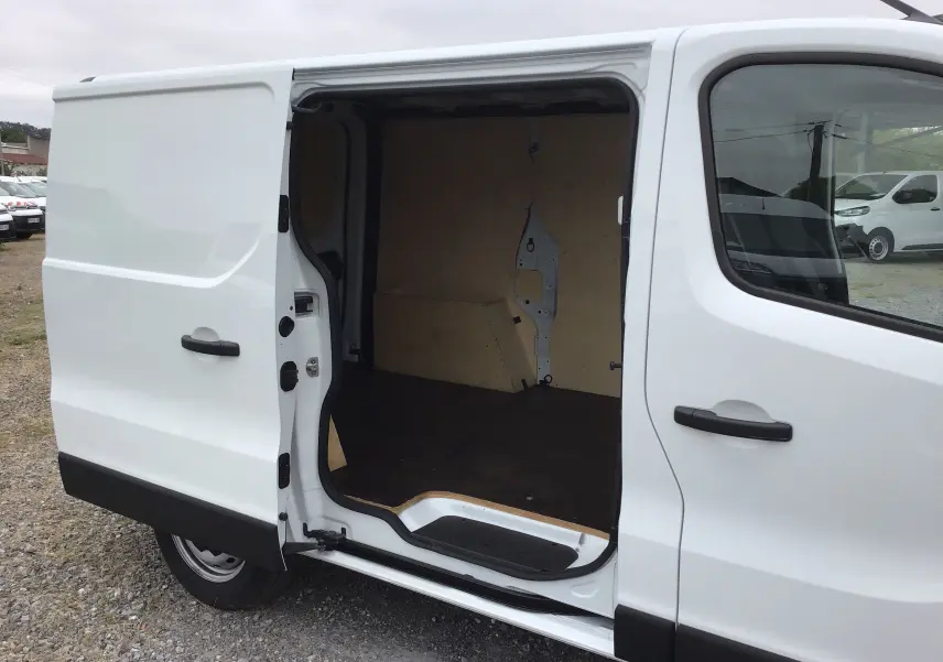 Vue latérale gauche d’un Renault Trafic Fourgon blanc 2024 avec porte coulissante ouverte montrant l’intérieur vide en bois.