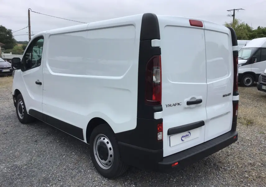 Vue 3/4 arrière droite du Renault Trafic Fourgon blanc 2024 avec portes arrière fermées et détails noirs contrastants.