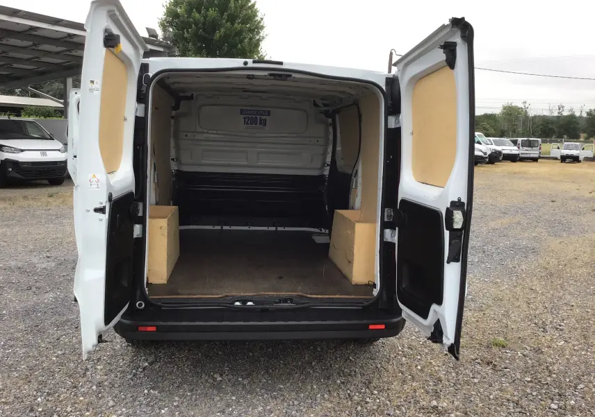 Vue arrière d’un Renault Trafic Fourgon blanc 2024 avec portes ouvertes montrant l’espace de chargement vide et protégé par des panneaux bois.