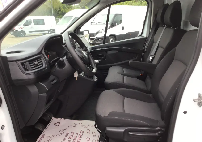 Vue intérieure côté conducteur du Renault Trafic Fourgon blanc 2024, montrant les sièges avant et le tableau de bord avec volant multifonction.