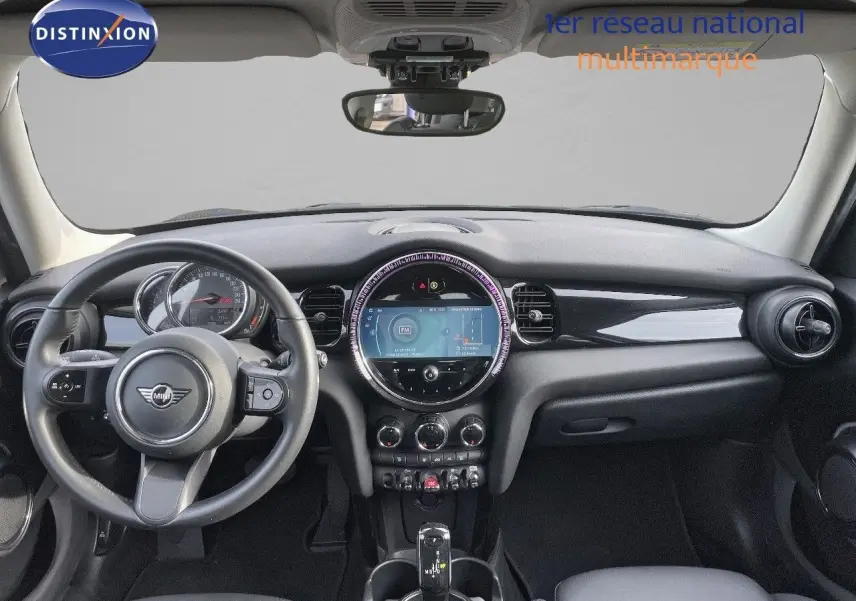 Vue frontale de l'habitacle d'une MINI 1.5 136CH noire avec tableau de bord moderne et écran central rond lumineux.