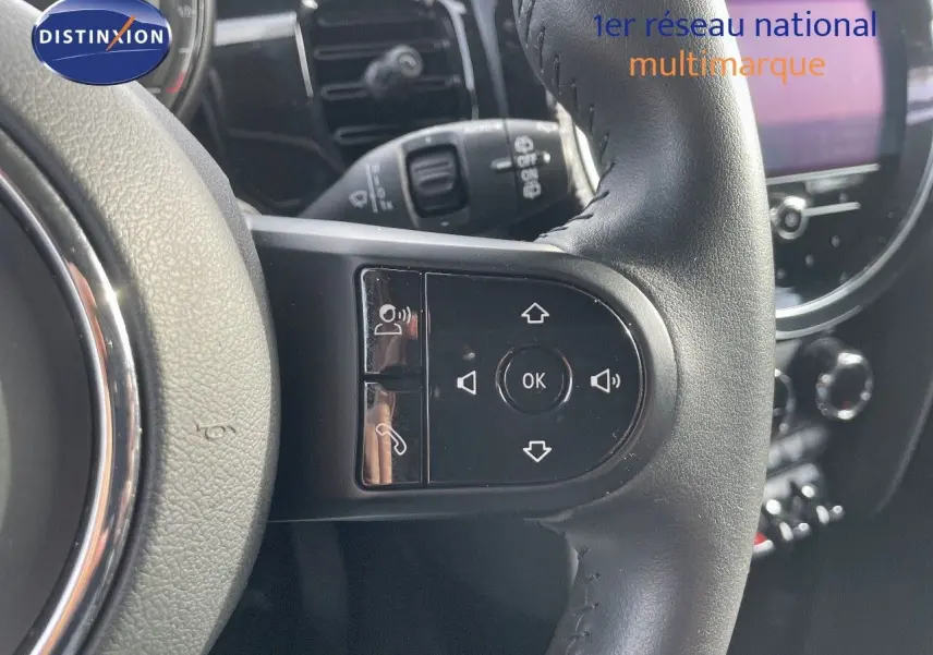 Gros plan sur le volant noir de la MINI 2023, mettant en valeur les commandes intégrées et l'écran de bord en arrière-plan.