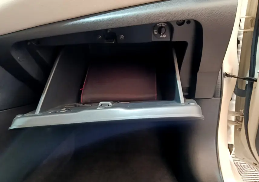 Gros plan sur la boîte à gants ouverte côté passager d'une Nissan Micra blanche, avec un manuel à l'intérieur.