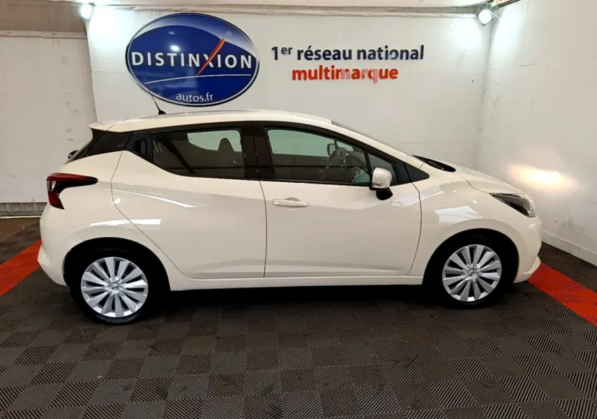 Profil côté droit d'une Nissan Micra IG-T 92 Acenta blanche 2022 dans un showroom avec logo Distinxion en arrière-plan.