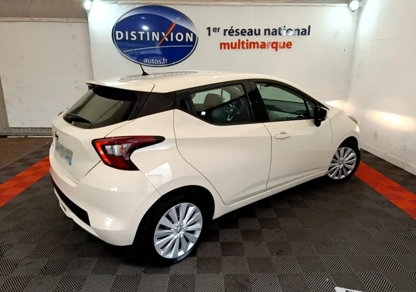 Vue 3/4 arrière droite d'une Nissan Micra blanche 2022 dans un showroom avec logo Distinxion en arrière-plan.