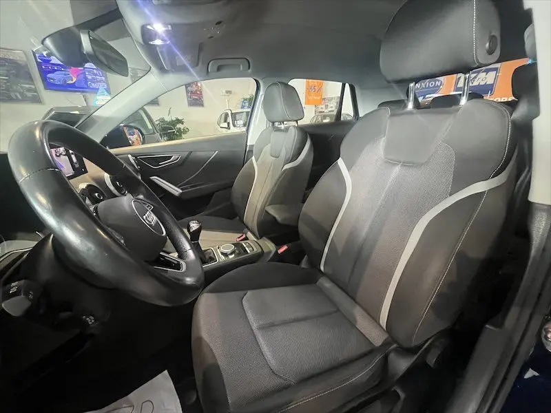 Intérieur de l'Audi Q2 30 TFSI S-Line 2021, vue côté conducteur, sièges sport noirs et volant cuir.