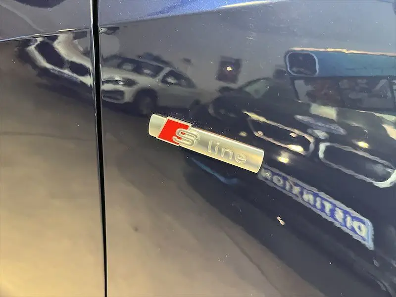 Gros plan sur l'écusson S line argent et rouge sur la porte bleu Navarre métallisé d'un Audi Q2 2021.