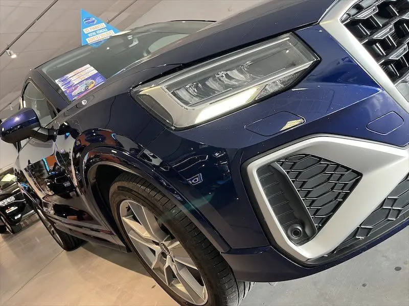Vue 3/4 avant droit d'un Audi Q2 30 TFSI S-Line bleu Navarre métal, mettant en valeur ses phares et jantes sport.
