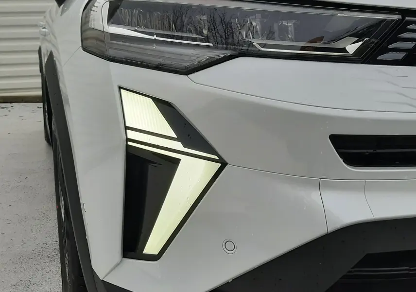 Gros plan sur l'avant gauche du Renault Symbioz blanc nacré, mettant en valeur son phare LED au design angulaire distinctif.