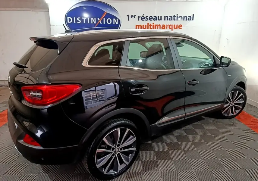 Vue 3/4 arrière droite du Renault Kadjar Intens noir brillant dans un showroom avec jantes alliage et vitres teintées.