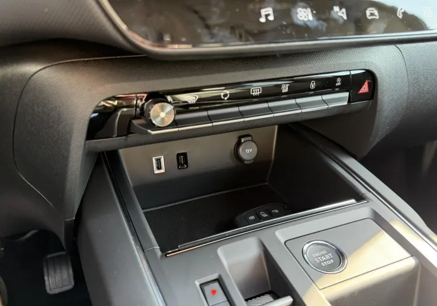 Vue rapprochée de la console centrale noire du Citroën C5 Aircross 2025 avec boutons de commande et prise 12V visible.