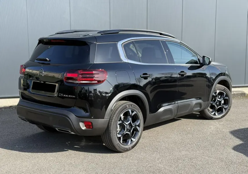 Vue 3/4 arrière droite d’un Citroën C5 Aircross 2025 noir Perla avec jantes alliage bi-ton et barres de toit noires.