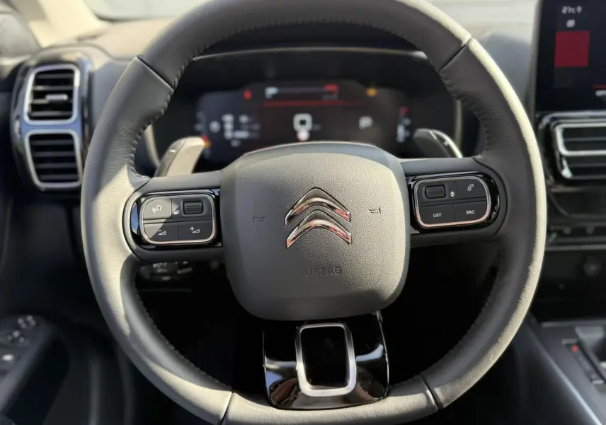 Vue rapprochée du volant en cuir noir du Citroën C5 Aircross 2025 avec commandes intégrées et tableau de bord numérique flou.