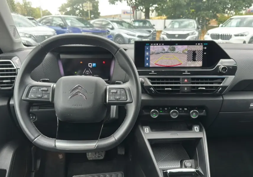 Vue intérieure centrée sur le volant cuir et l'écran tactile affichant la caméra de recul d'une Citroën C4 gris 2024.