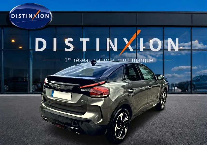 Vue 3/4 arrière droite d'une Citroën C4 gris métallisé avec jantes alu, garée devant une vitrine Distinxion.