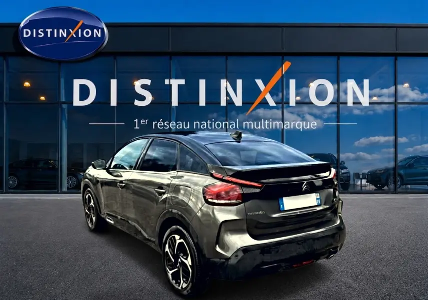 Vue 3/4 arrière droite d'une Citroën C4 gris métallisé avec jantes alliage, garée devant une vitrine Distinxion.