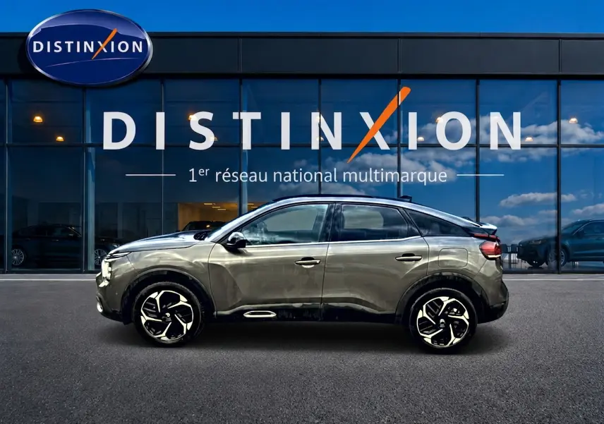 Profil côté gauche d'une Citroën C4 gris 2024 avec jantes alliage, devant une vitrine Distinxion.