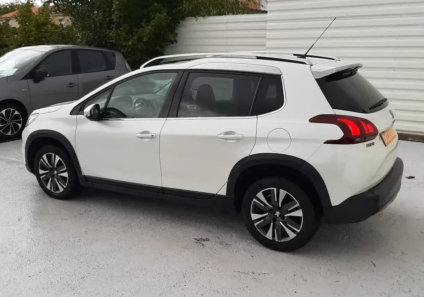 Peugeot 2008 blanc vue 3/4 arrière côté gauche, avec jantes alliage bi-ton et feux arrière LED allumés.