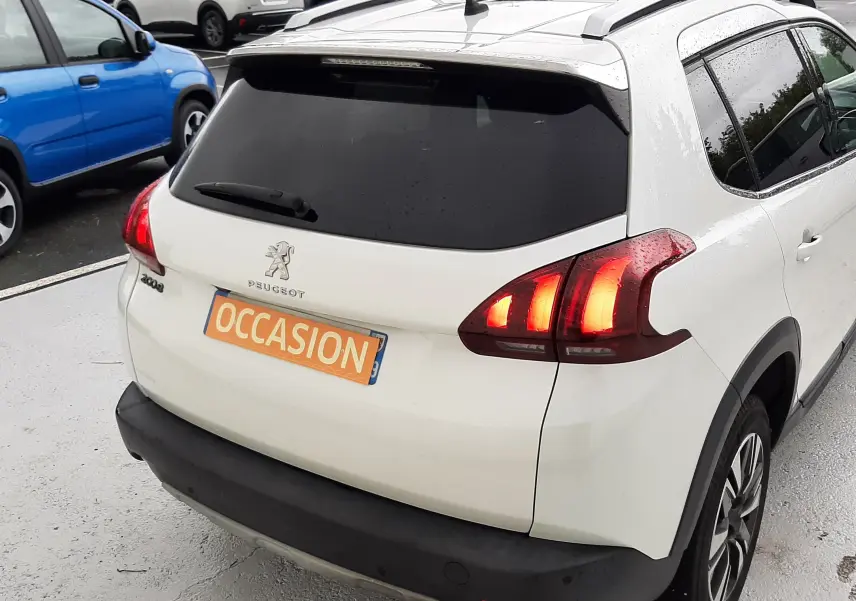 Vue 3/4 arrière droite d'un Peugeot 2008 blanc de 2017 avec feux arrière allumés et plaque "OCCASION" visible.