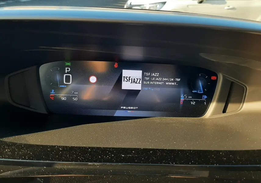 Tableau de bord numérique de Peugeot 308 Bleu Obsession, affichant la radio TSF Jazz en plein jour.