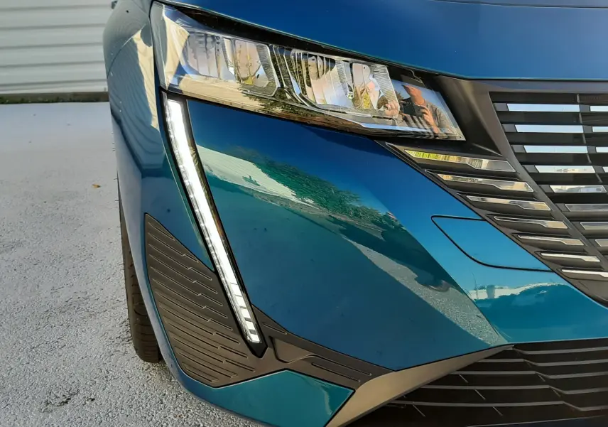 Gros plan sur l'avant gauche bleu obsession de la Peugeot 308 2025, mettant en valeur le phare et la calandre distinctive.