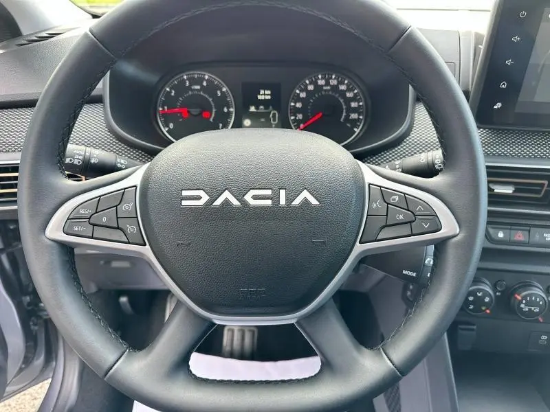 Vue rapprochée du volant noir du Dacia Sandero 2025 avec commandes intégrées et tableau de bord visible en arrière-plan.