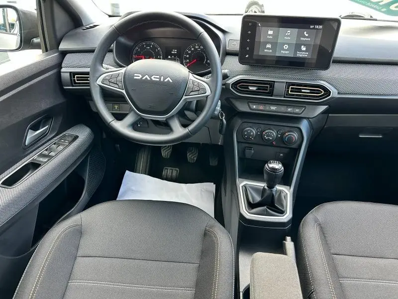 Vue intérieure avant de la Dacia Sandero 2025 blanche, volant multifonction, écran tactile et boîte manuelle visible.