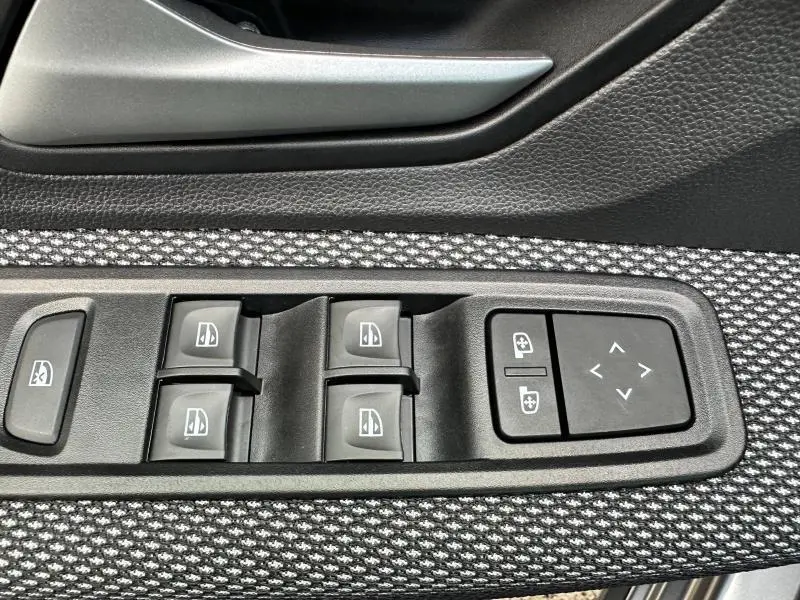 Détail des commandes des vitres électriques et réglages des rétroviseurs sur la porte côté gauche d'une Dacia Sandero blanche.