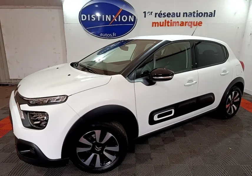 Citroën C3 blanche vue 3/4 avant droit, avec protections latérales noires et jantes bi-ton modernes.