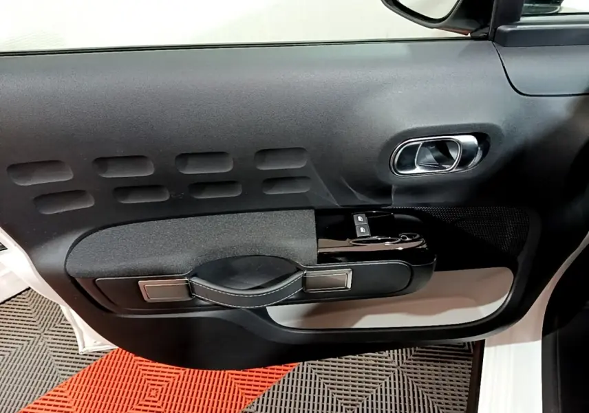 Vue intérieure côté gauche de la porte avant d'une Citroën C3 blanche avec poignée noire et commandes de vitres.
