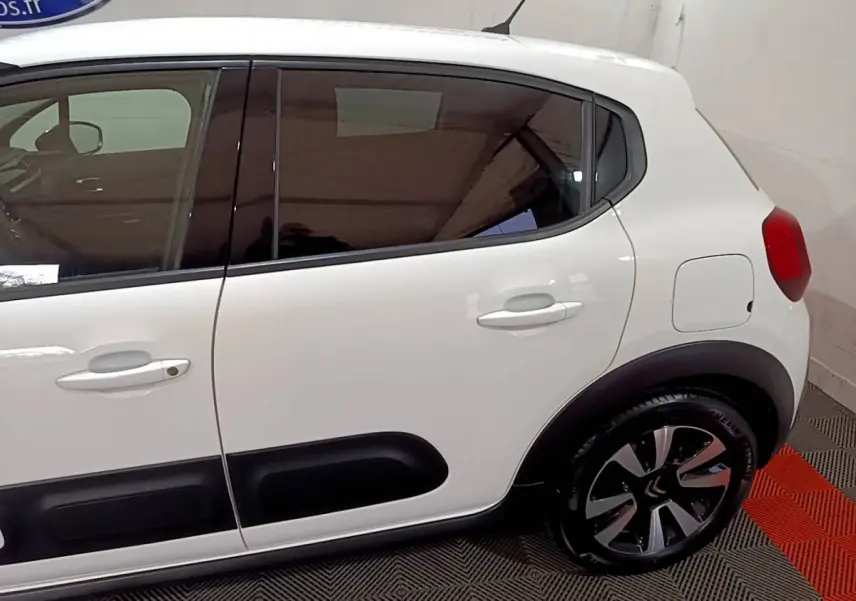 Vue latérale droite sur la partie arrière d'une Citroën C3 blanche avec protections noires et jantes stylisées.