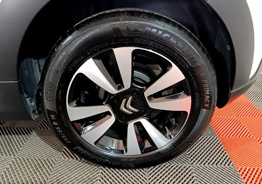 Gros plan sur la jante alliage noire et argentée d'une Citroën C3 blanche, roue avant droite visible.