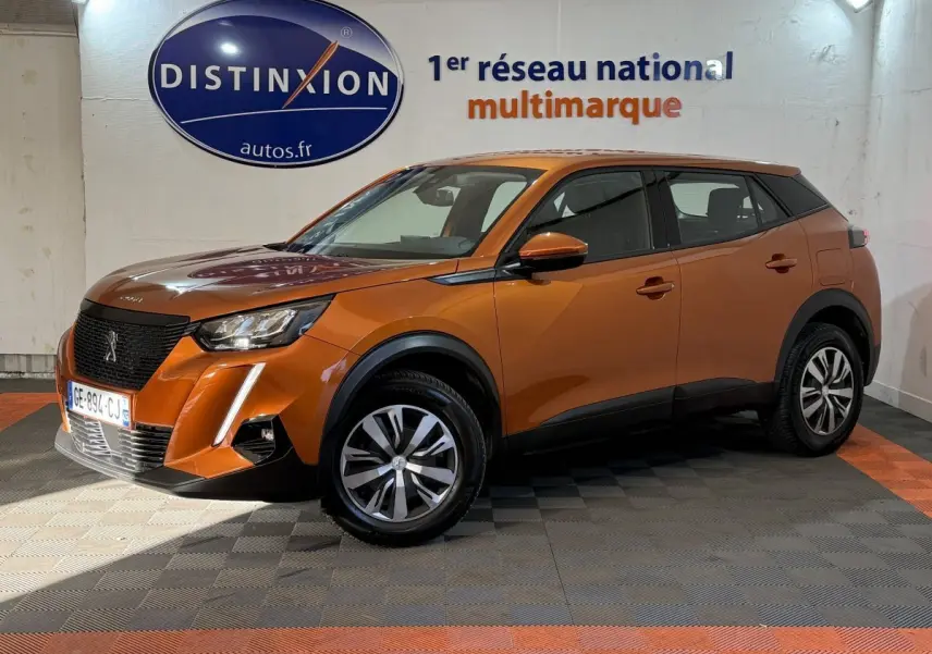 Peugeot 2008 orange vue 3/4 avant droit en intérieur, avec calandre noire et jantes bicolores.