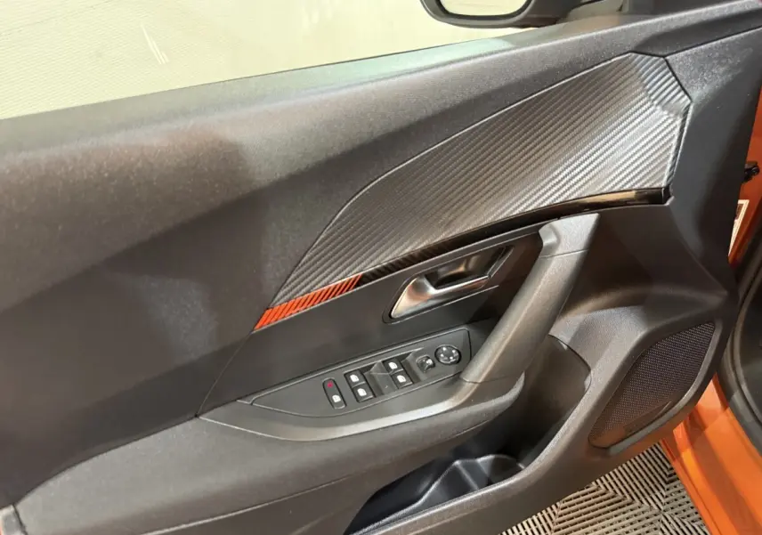 Vue intérieure du panneau de porte côté conducteur du Peugeot 2008 orange 2022 avec insert décoratif carbone et commande des vitres.