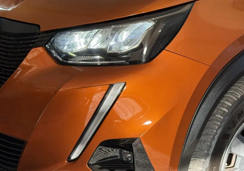 Gros plan sur le phare avant droit et la calandre d’un Peugeot 2008 orange métallisé avec antibrouillard intégré.