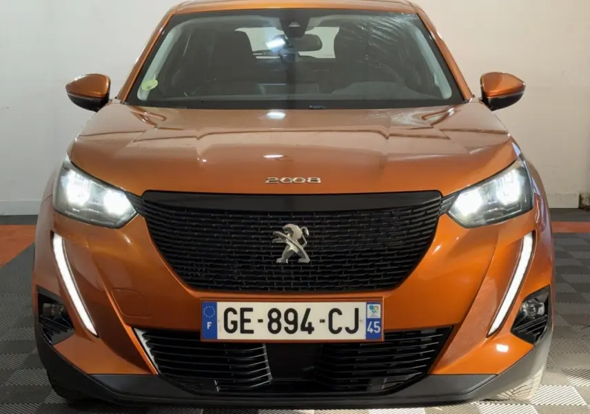 Vue avant d’un Peugeot 2008 orange 2022 avec phares allumés et calandre noire distinctive.