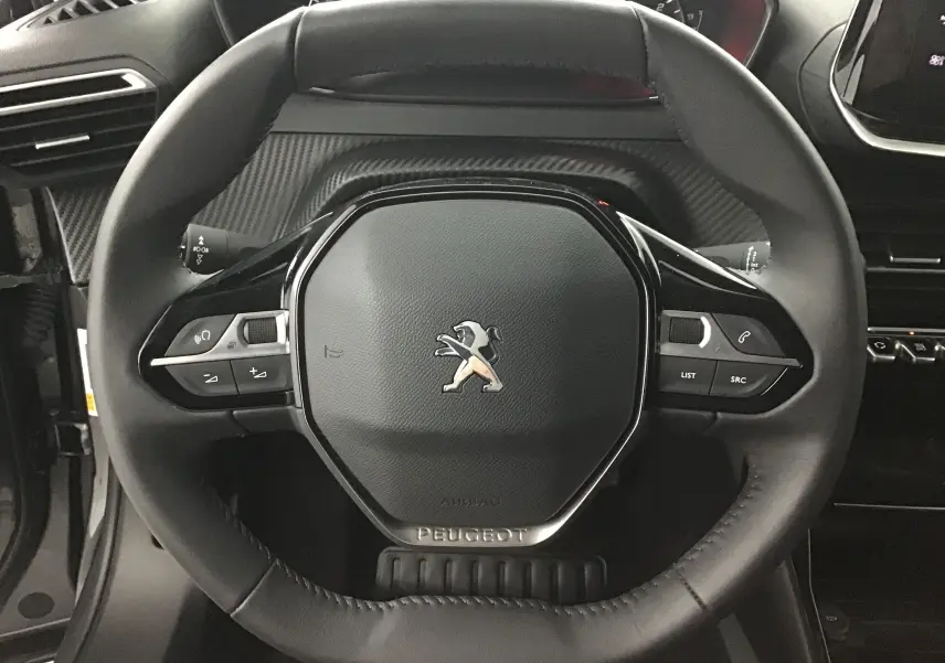 Gros plan sur le volant cuir noir du Peugeot 2008 1.2 PureTech 100 Allure 2022 avec commandes intégrées et logo lion central.