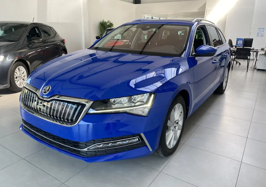 Vue 3/4 avant droite d'une Skoda Superb Combi IV bleu énergie en showroom avec calandre chromée et phares LED.