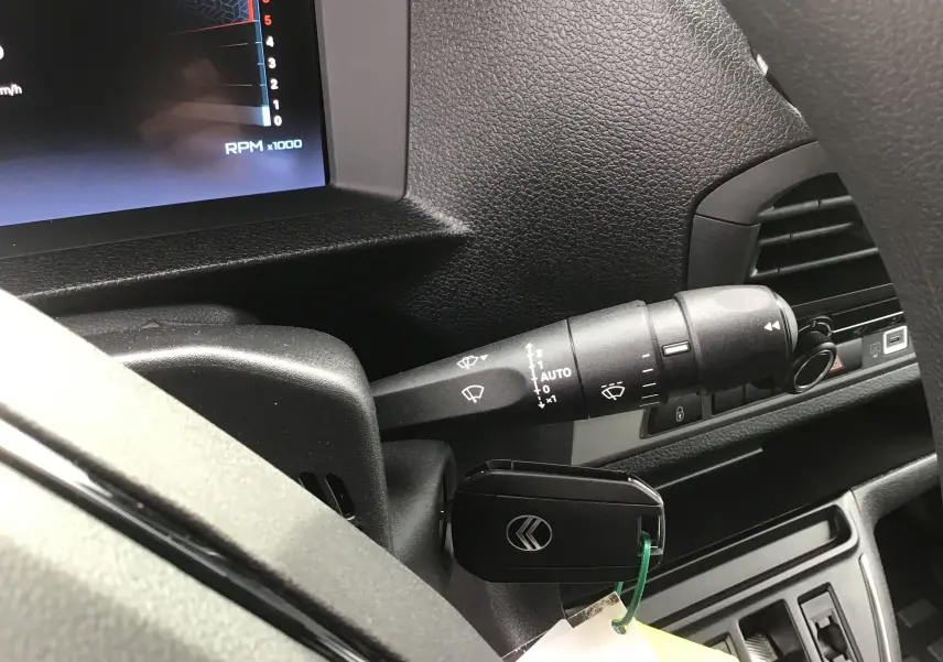 Gros plan sur la manette d'essuie-glace et la clé de contact dans le tableau de bord noir du Citroën Jumpy cabine approfondie blanc.