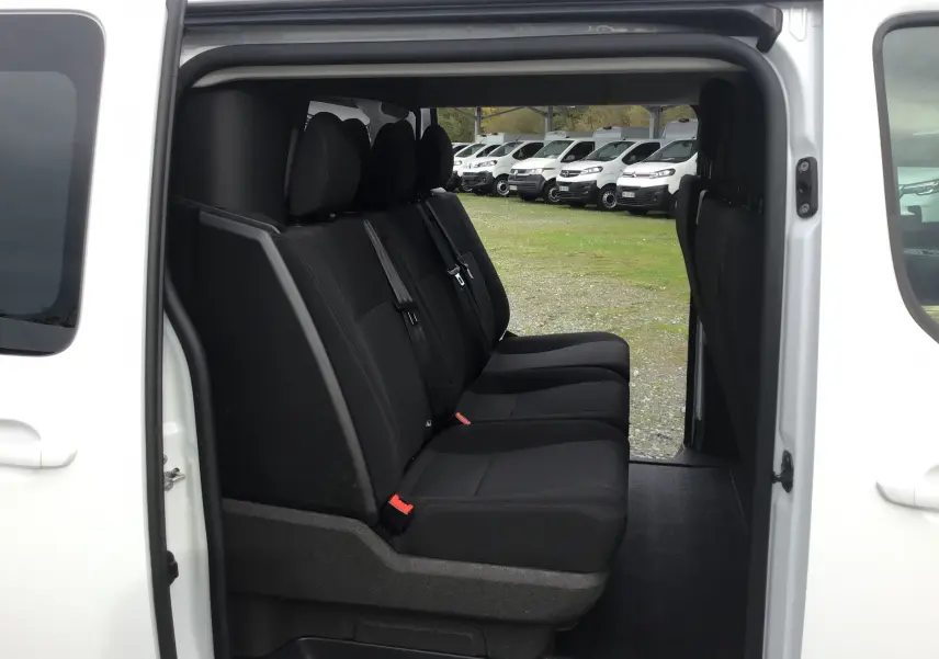 Vue latérale intérieure des sièges noirs du Citroën Jumpy Cabine Approfondie blanc avec porte coulissante ouverte.