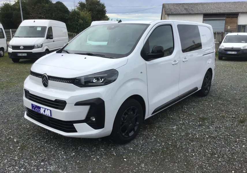 Vue 3/4 avant droite d'un Citroën Jumpy blanc avec calandre noire et jantes foncées sur un sol gravillonné.