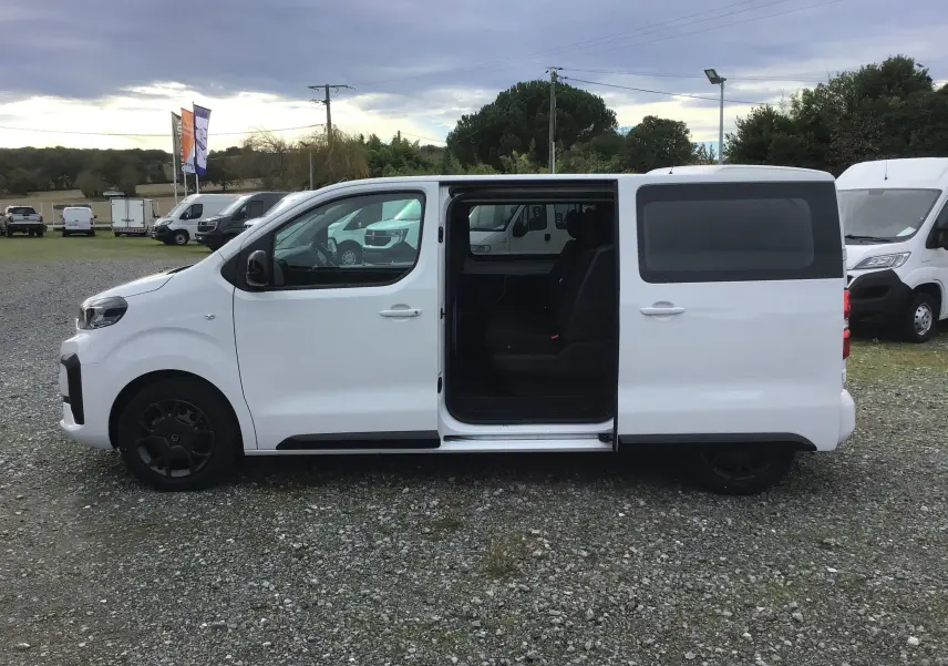 Vue de profil côté gauche d'un Citroën Jumpy cabine approfondie blanc avec porte coulissante ouverte révélant l'intérieur noir.