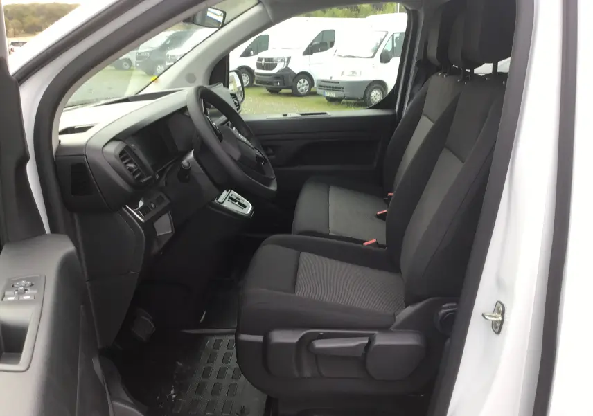 Intérieur côté conducteur du Citroën Jumpy blanc, montrant les sièges avant et le tableau de bord depuis la porte ouverte.
