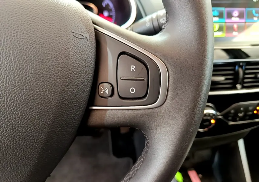 Gros plan sur le volant cuir noir de la Renault Clio Business TCe 90 avec commandes vocales et tableau de bord tactile en arrière-plan.